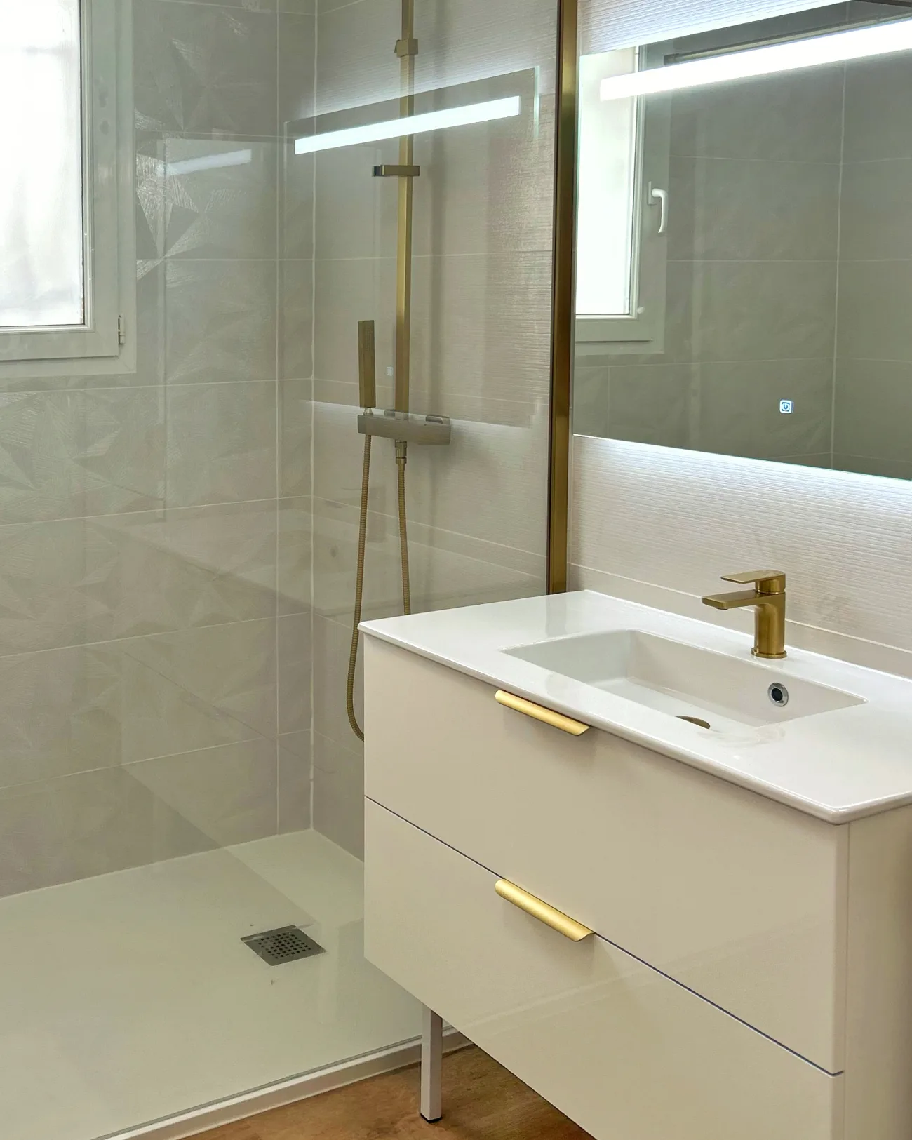 Salle de bain rénovée par RECB82 à Montauban : douche à l’italienne, robinetterie dorée, miroir rétroéclairé et meuble suspendu