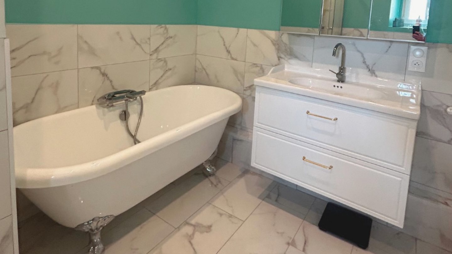 La même salle de bain après rénovation par RECB82 : carrelage effet marbre, baignoire îlot remise à neuf et meuble suspendu